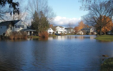 A serene neighborhood scene with houses reflecting in a flooded area, showcasing nature's impact on urban life.