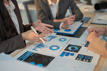 Businesswomen are having a meeting, discussing and analyzing charts and graphs, using a pen to point at specific data points on printed documents