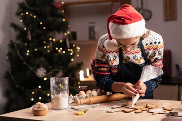 Young woman in Santa hat cooking and decorating Christmas cookies in her kitchen.