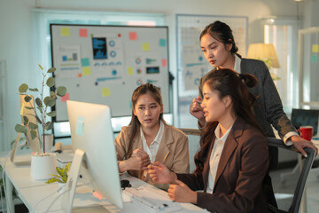 Three asian businesswomen are working together on a computer in a modern office, discussing a new project and explaining strategy and planning operations