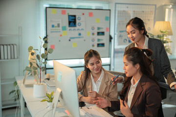 Three asian businesswomen are working together in the office, discussing a project on a desktop computer, collaborating and sharing ideas in a productive teamwork environment