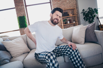 Obraz premium Photo of upset sad guy wear sleepwear pajama sitting home sofa having back ache indoors house apartment room