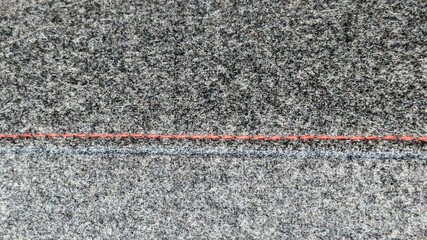 Red thread is stitched through gray flannel horizontally. Fabric furniture background