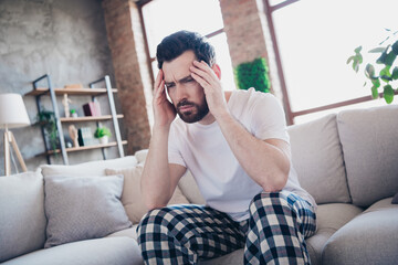 Photo of sick sad man wearing pajama staying home feeling unwell sitting on sofa living room indoors