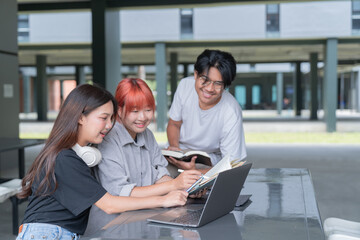 Group of smiling young asian students working together on a school assignment, using a laptop and...