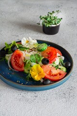 Appetizing salad with feta cheese, fresh vegetables (tomatoes, cucumbers, onions), crispy lettuce, microgreens and violet flowers. Non-standard serving of Greek salad.