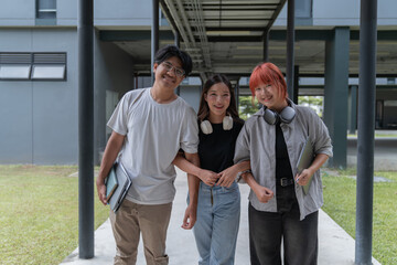 Three happy asian students walking on campus, holding laptops and books, enjoying university life. Smiling and embracing modern learning, showcasing teamwork and diversity