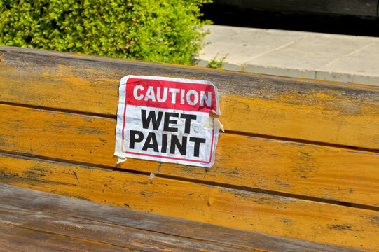 Caution wet paint sign taped onto a wooden beanch in a public park. No people.