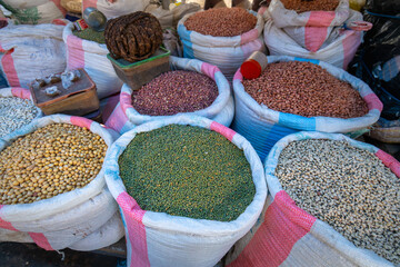 A vibrant display of colorful grain sacks filled with various legumes, such as green mung beans, soybeans, and peanuts, at a local market in Morondava, Madagascar.