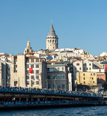 Obraz premium A stunning panoramic view of Istanbul's Galata Tower with its distinctive conical roof and pointed spire. It is surrounded by a lively urban landscape with a mix of traditional and modern architecture