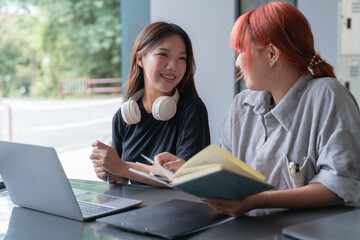 Two young female students collaborating on a project, discussing and using a laptop in a modern learning environment