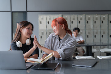 Two happy female students are giving high five while studying together in the library, celebrating their academic achievement or project milestone