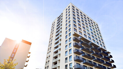 Fototapeta premium Modern high-rise apartment building in white, stand tall against a blue sky, exemplifying innovative urban architecture with sleek, angular designs.