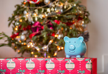 Blue piggy bank front of a Christmas tree decorated with beautiful Christmas vibes. Holiday season in December for family and friends together and give a gift and using money. saving money for present