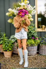 A woman hides her face behind a vibrant bouquet of garden flowers, capturing the essence of a...