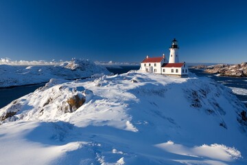 A picturesque winter landscape featuring a lighthouse surrounded by snow-capped mountains and a clear blue sky during the daytime