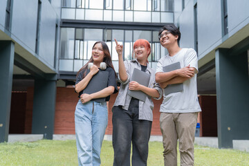 Obraz premium Three cheerful asian university students holding laptops and folders are discussing and pointing while walking on campus