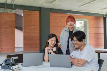 Three young asian students are working together on their laptops, enjoying a collaborative learning experience in a modern university environment