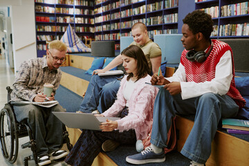 Group of students collaborating in modern library setting, with one student in wheelchair holding a...