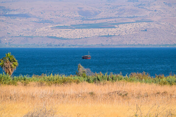 The holy Sea of Galilee in summer - a red boat in the middle of the Sea of Galilee in northern Israel, with the Golan Heights in the background