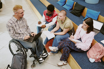 Group of diverse university students engaging in studying, sitting on campus steps, with notes and...