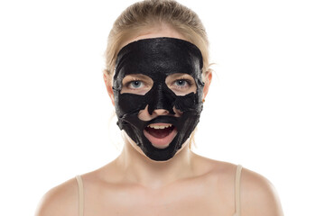 Beautiful young happy woman posing with a facial black paper mask on her face. Skin care and treatment, spa, natural beauty and cosmetology concept