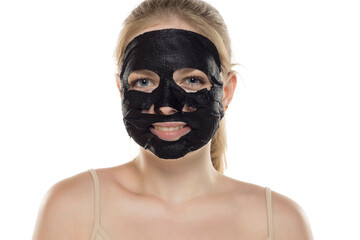 Beautiful young smiling woman posing with a facial black paper mask on her face. Skin care and treatment, spa, natural beauty and cosmetology concept