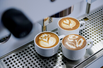 Three latte art cups with different designs placed against a coffee maker.Using skills in making latte menus.Drink coffee in the morning.
