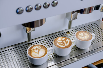 Three latte art cups with different designs placed against a coffee maker.Using skills in making latte menus.Drink coffee in the morning.
