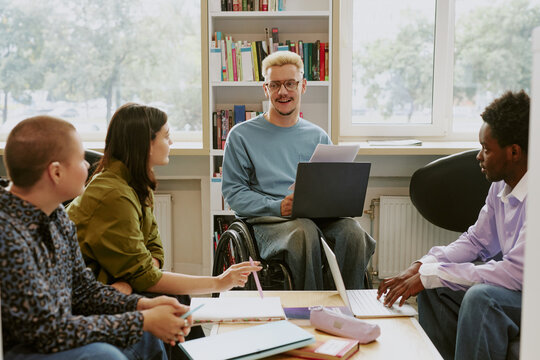 Group of four diverse colleagues discussing business strategy in office setting with laptop and documents, fostering team collaboration and inclusion