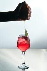 Hand Pressing Orange over Raspberry Red Cocktai