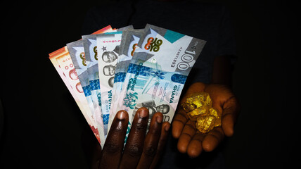 Person holding Ghana Cedis notes and gold lumps nuggets flakes in her hand over dark background.