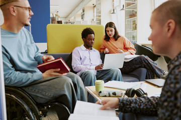 Young professionals working together in modern office space with diverse team members collaborating on project and using laptops and tablets