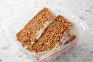 A closeup view of a slice of carrot cake in a plastic container.