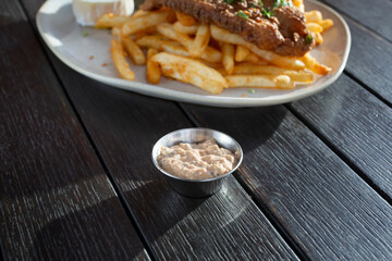 A view of a metal condiment cup of tartar sauce, with a fried catfish entree.