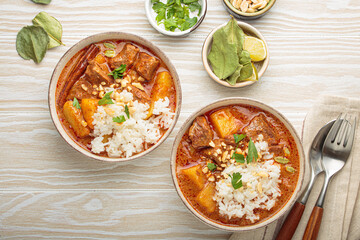 Two bowls of rich and flavorful massaman curry are served with beef, potatoes, and fluffy white rice, topped with crunchy peanuts and fresh parsley, a vibrant and aromatic thai dish