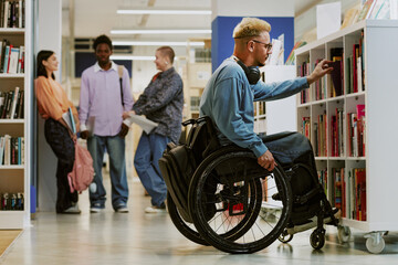 Person in a wheelchair browsing books at a modern library, with diverse group of people engaging in background activities shelving books and discussing literature