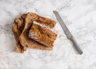 Sliced loaf of bread with a silver knife on the side. Flat lay of cut bread on a marble counter. 