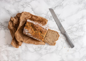 Sliced loaf of bread with a silver knife on the side. Flat lay of cut bread on a marble counter. 