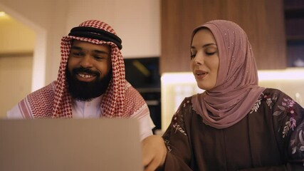 Cheerful Muslim couple booking hotel for vacation on laptop, family pastime