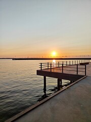 Obraz premium A serene sunset in Helsingborg over the water, with a wooden pier extending into the calm sea, creating a peaceful and scenic view