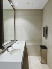 This welldesigned bathroom features a spacious layout with two sinks, a large mirror for grooming, and a strategically placed trash can for cleanliness and organization