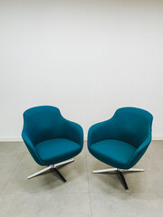 In a cozy and inviting setting, two vibrant blue chairs are artfully positioned together in front of a pristine clean white wall that beautifully complements their striking and bold color