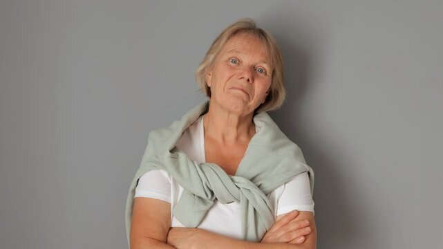 Satisfied senior woman smiling and nodding her head in agreement expressing her approval and satisfaction with deal while posing against gray background