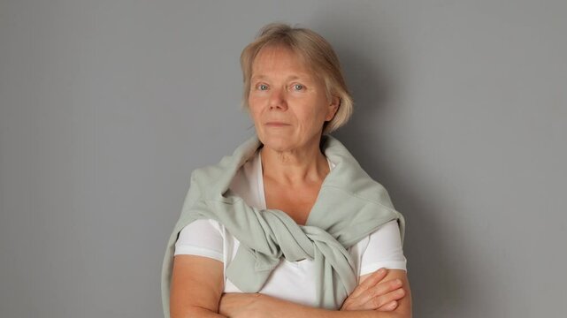 Senior woman with confident expression shaking head in denial refusing to agree with negative statements nodding no to suggestions and showing dislike for proposal isolated over gray background