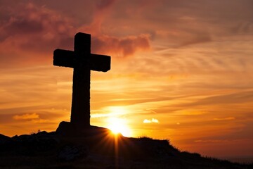 Silhouette of stone cross against vibrant sunset with dramatic sky