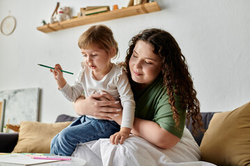A loving mother cuddles her daughter as they engage in colorful artistic activities on a cozy couch.