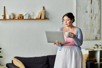 A plus size woman interacts with her laptop, holding a mug, in a comfortable home setting.