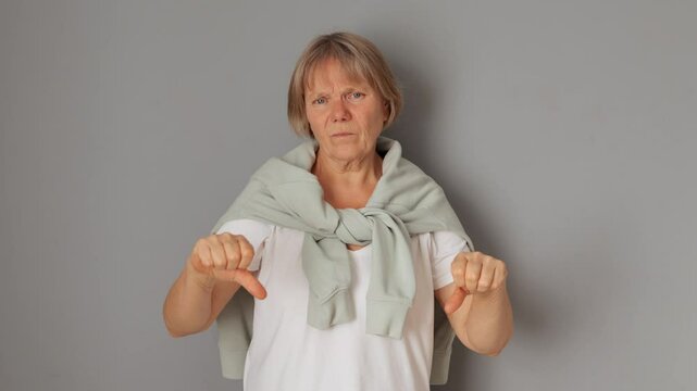 Uncertain mature woman showing signs of doubt and disinterest feeling hunched and puzzled by unknown question indicating her indifference shrugging shoulders isolated over gray background