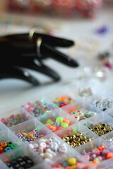 Hand figurine, colorful friendship bracelets, necklaces, various beads and DIY supplies on the table. Making jewelry at home. Selective focus.